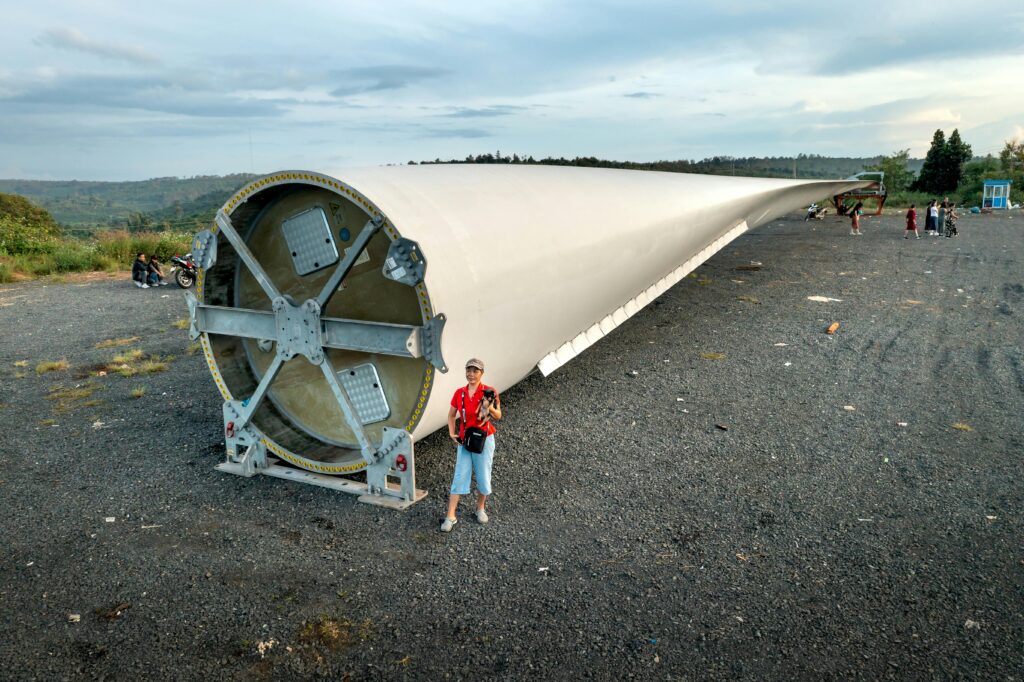 A massive wind turbine blade lying outdoors with people nearby for scale.