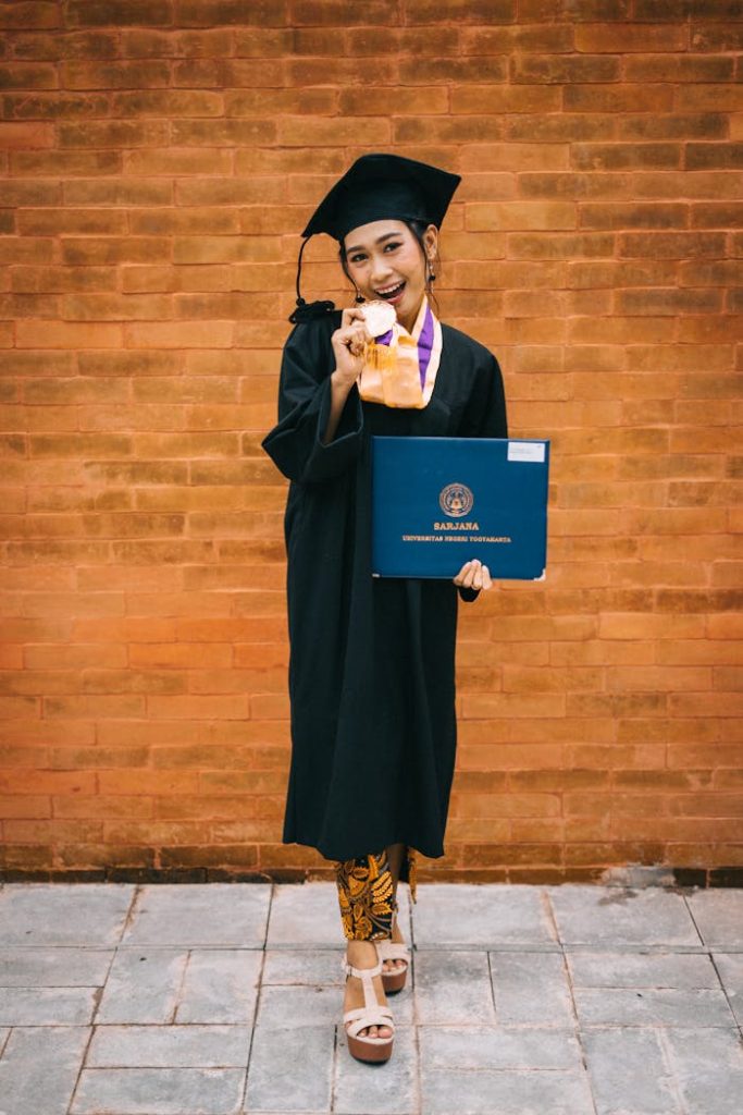 Joyful graduate in cap with diploma and medal against brick wall backdrop.